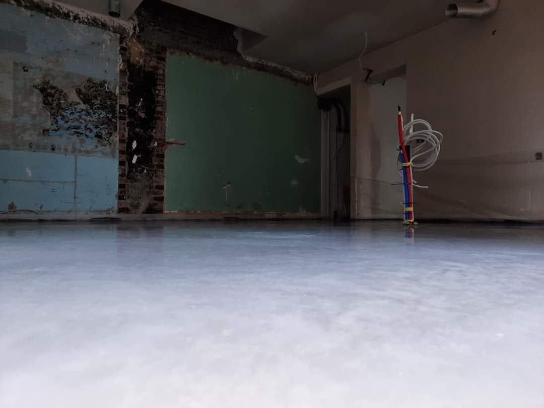 Świeżo wylana, gładka wylewka samopoziomująca w surowym wnętrzu z instalacją elektryczną. Widoczne ślady po remoncie na ścianach.