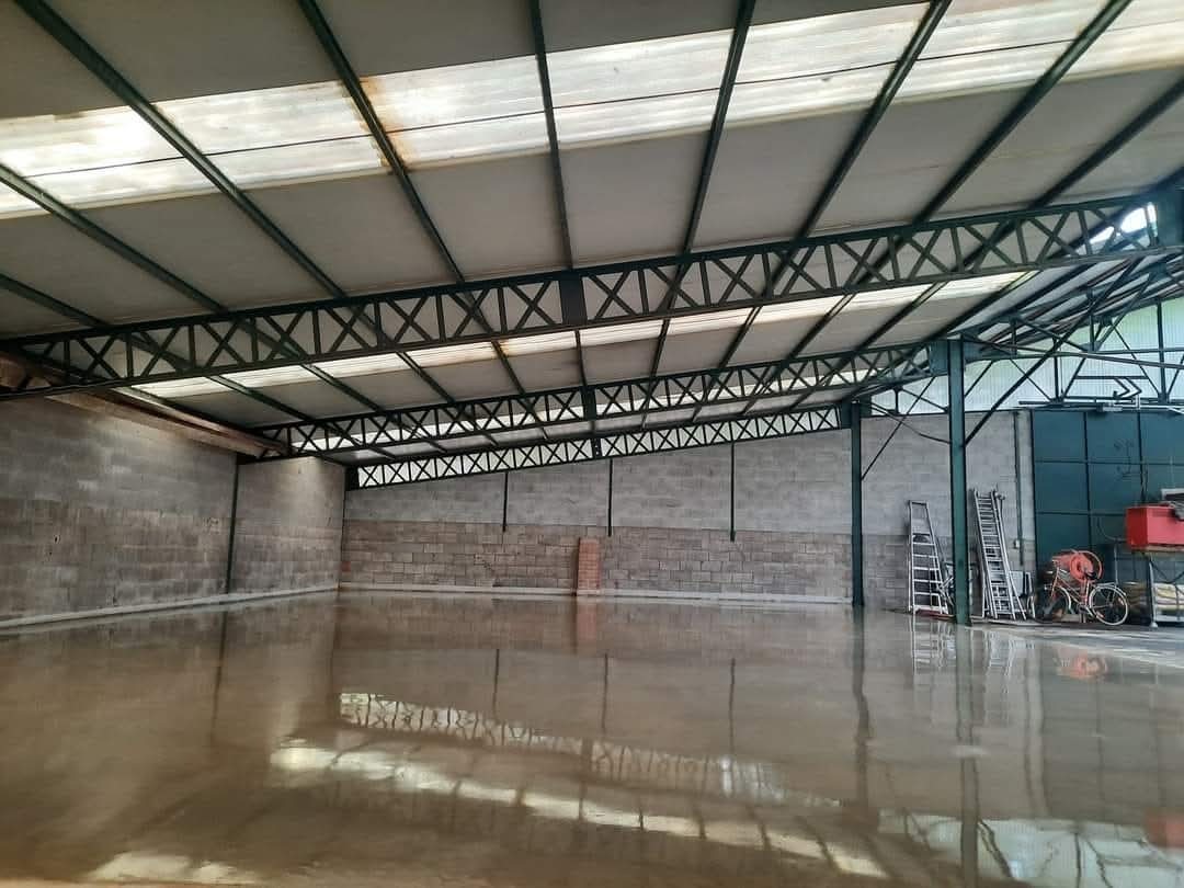 Gładka, mokra powierzchnia w hali z betonowych bloków, odbijająca metalową konstrukcję dachu. Widoczne drabiny i sprzęt budowlany w tle.