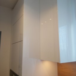 Tomek Banasiak - Białe, lakierowane szafki kuchenne pod sufit, z delikatnym oświetleniem podszafkowym, tworzące minimalistyczny i nowoczesny design kuchni. Widok z dołu.