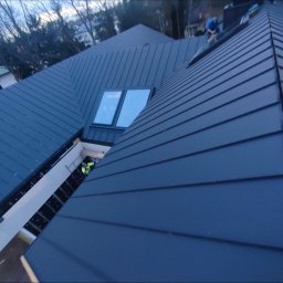 LEONID VASHCHENKO - Nowoczesny, grafitowy dach z blachy na rąbek stojący, z oknami dachowymi. Widoczni dekarze podczas prac montażowych, z góry.