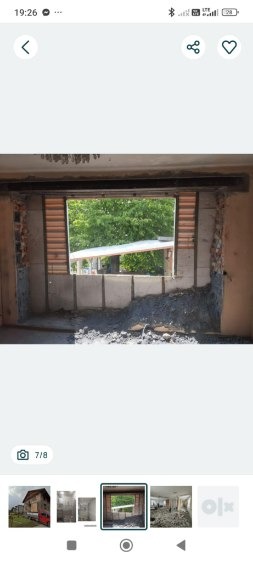 Otwór po wyburzonej ścianie z widocznymi elementami konstrukcyjnymi i gruzem. Widok na zieleń przez otwór. Etap prac przygotowawczych do dalszych działań budowlanych.