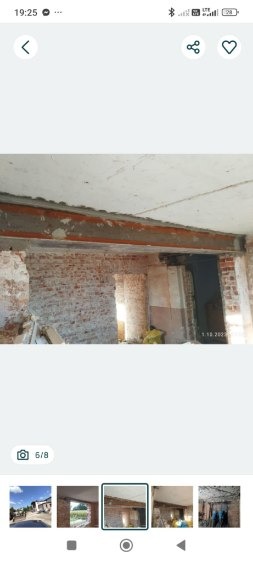 Ceglana ściana z widocznymi śladami po usuniętych elementach, wzmocniona belką pod stropem. Widoczne fragmenty gruzu i odsłonięta konstrukcja budynku.