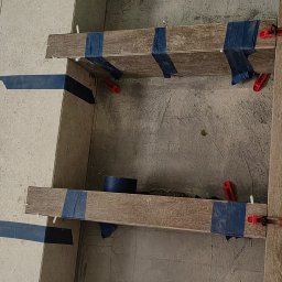 Wykończenia wnętrz Krystian Troska - Półki z płytek imitujących drewno, mocowane taśmą i poziomowane, w trakcie prac wykończeniowych w łazience w Katowicach. Widoczne narzędzia glazurnicze.