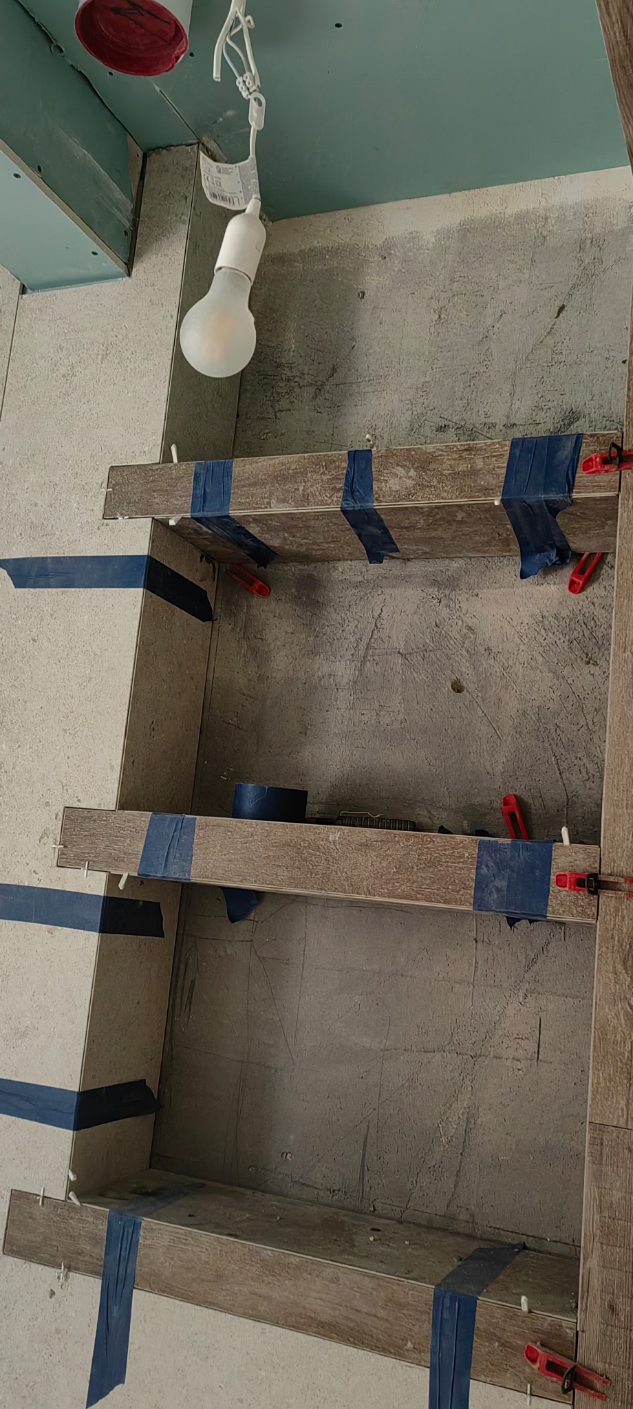 Półki z płytek imitujących drewno, mocowane taśmą i poziomowane, w trakcie prac wykończeniowych w łazience w Katowicach. Widoczne narzędzia glazurnicze.