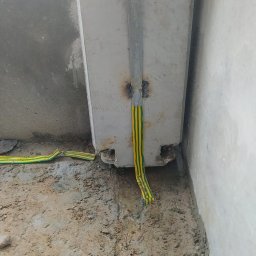 ADVOLT - Uziemienie budynku w trakcie budowy: żółto-zielony przewód przymocowany do metalowej szyny na betonowym słupie, widoczne spawy i wykop w ziemi.