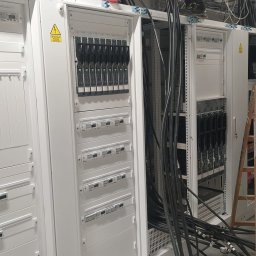ADVOLT - Rozdzielnice elektryczne w białych obudowach, widoczne kable i drabiny, sugerujące prace instalacyjne w dużej serwerowni lub obiekcie przemysłowym.
