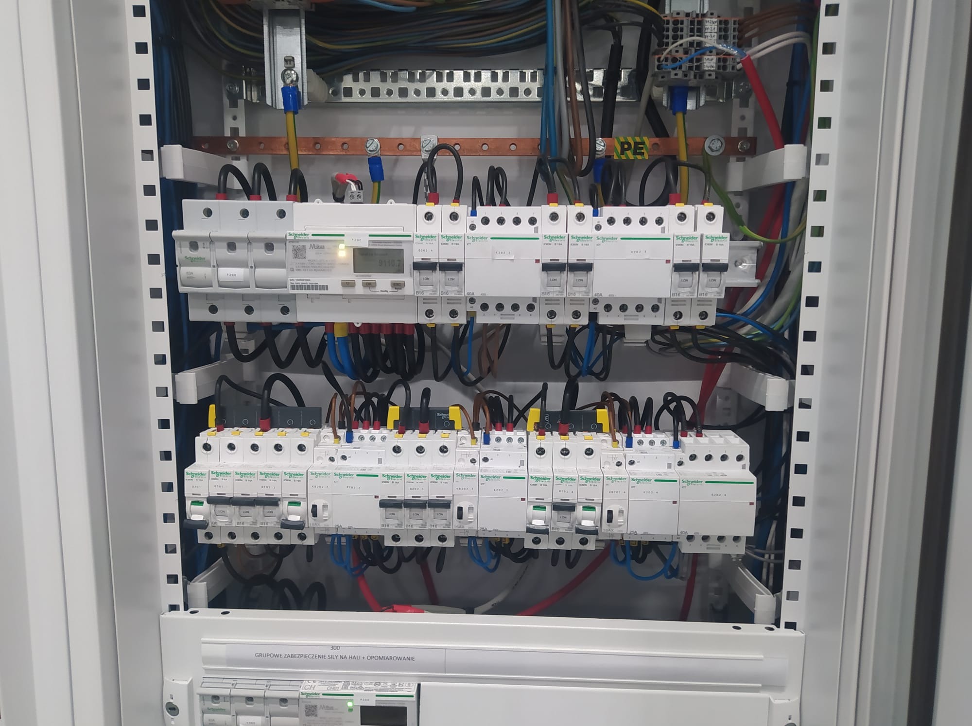 Rozdzielnica elektryczna z zainstalowanymi bezpiecznikami i przewodami. Widoczne elementy opomiarowania i zabezpieczenia siły na hali. Estetyczne i profesjonalne wykonanie.