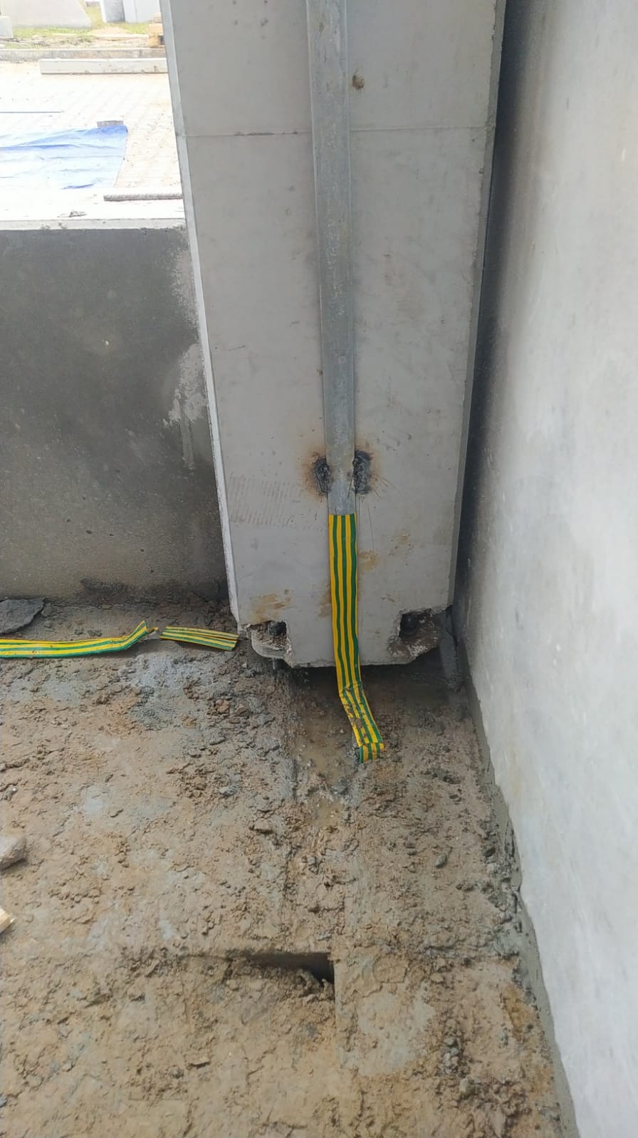 Uziemienie budynku w trakcie budowy: żółto-zielony przewód przymocowany do metalowej szyny na betonowym słupie, widoczne spawy i wykop w ziemi.