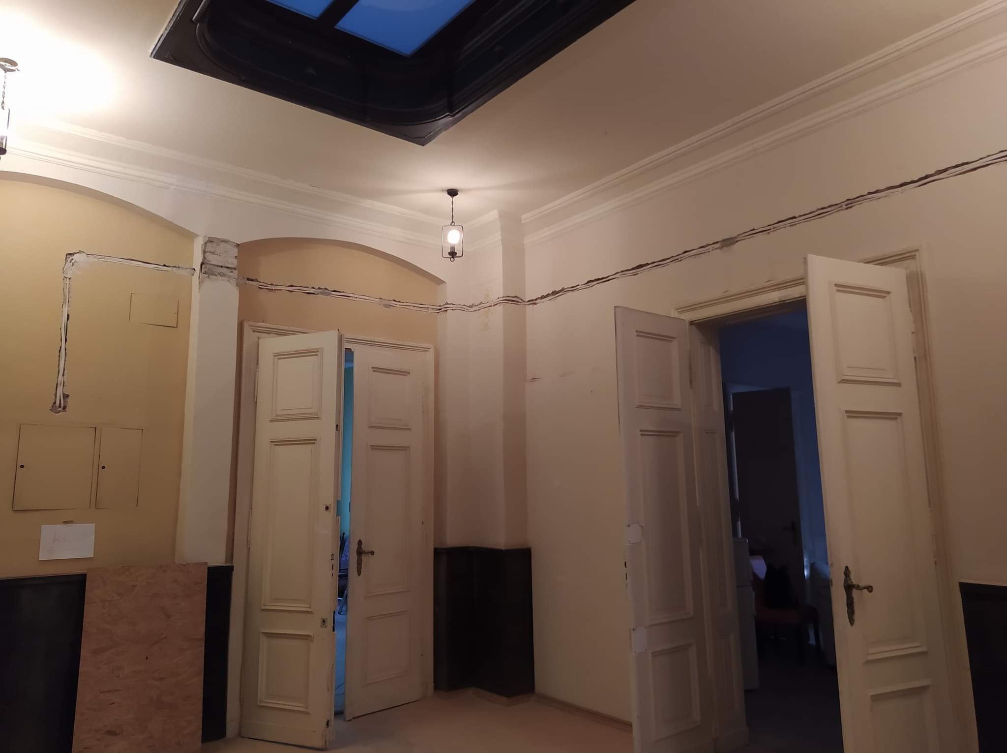 Wnętrze w trakcie remontu: widoczne bruzdy na ścianach pod instalacje elektryczne, otwarte drzwi i sufit z oknem dachowym. Etap prac przed wykończeniem.