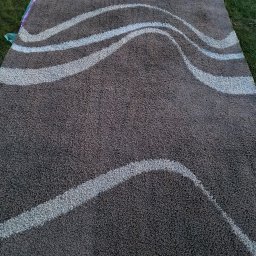 Clinex Paulina Ciak - Brązowy dywan z wzorem fal na trawie w Jeleniej Górze, przygotowany do transportu. Widoczne zabezpieczenia z folii i tkaniny. Usługa czyszczenia dywanów.