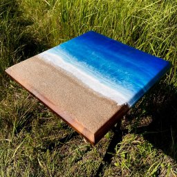 Pawel koscinski - Kwadratowy stolik kawowy z blatem imitującym plażę i morze, wykonany z żywicy epoksydowej i drewna, ustawiony na trawie w słoneczny dzień.