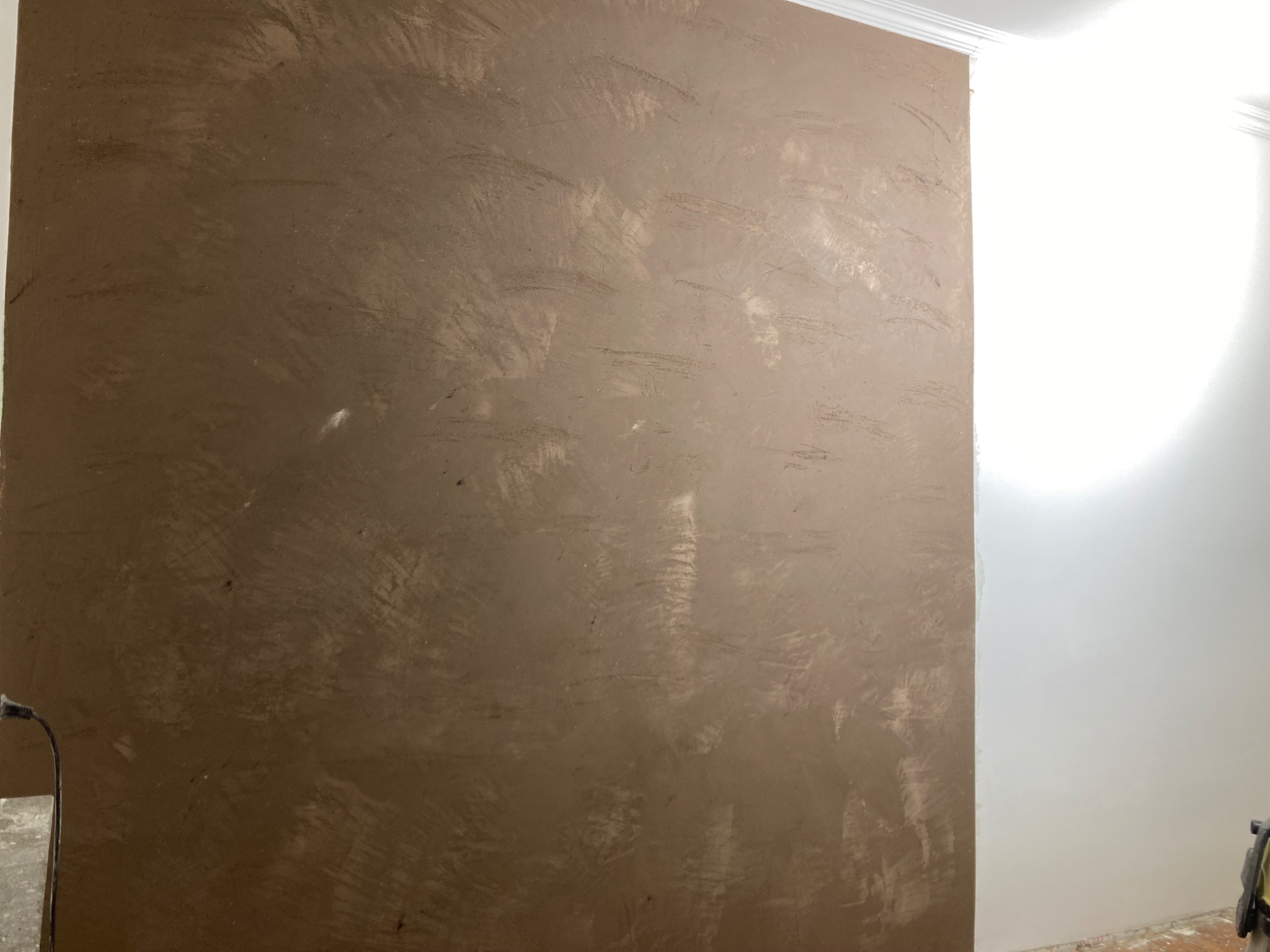 Ściana po szpachlowaniu z widoczną fakturą i śladami narzędzi, przygotowana do malowania. Fragment listwy przypodłogowej w rogu.