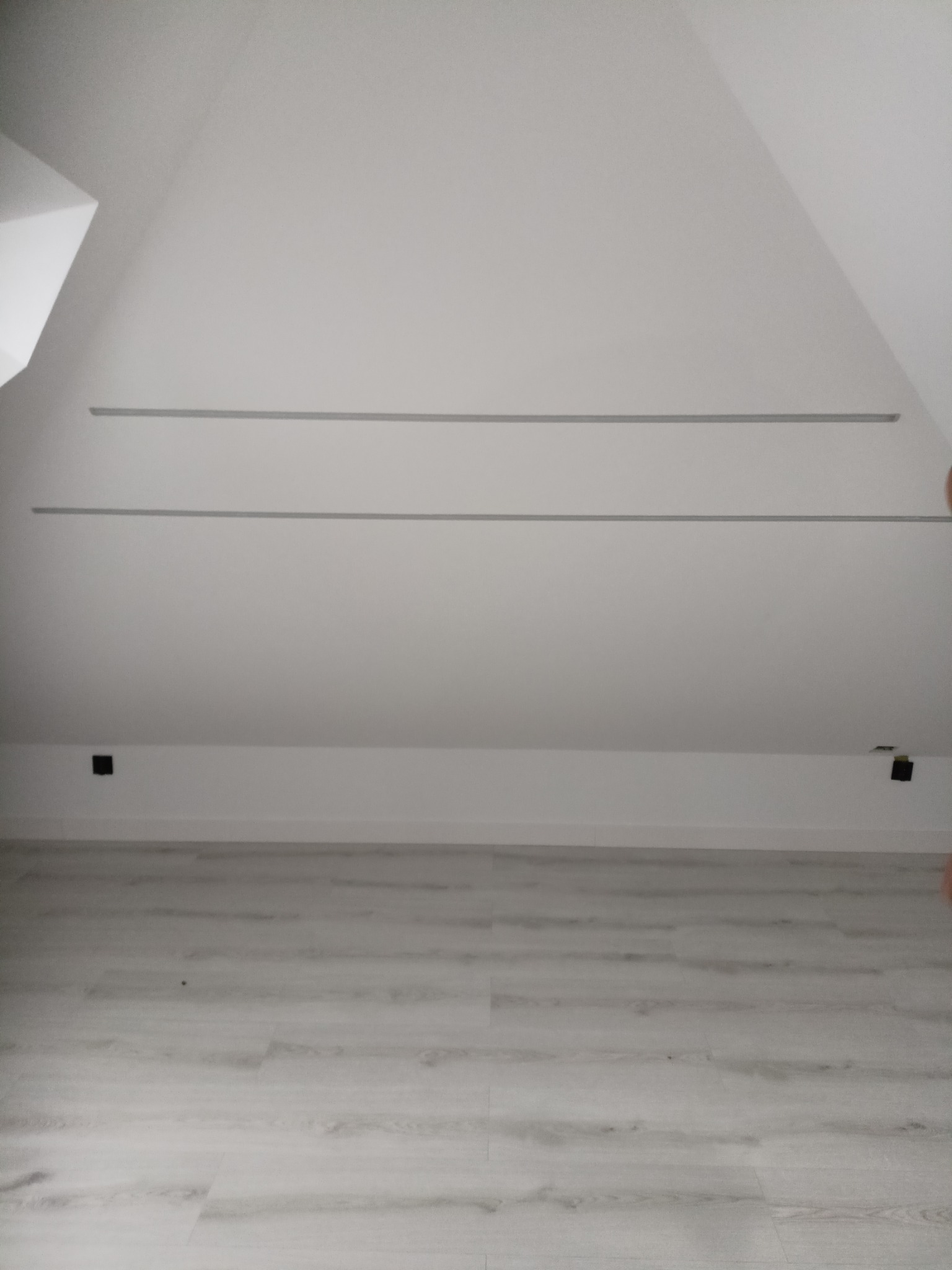 Wnętrze poddasza po remoncie we Wszeborach: białe ściany, jasna podłoga, widoczne listwy i gniazdka elektryczne. Skos dachu i minimalistyczny styl.