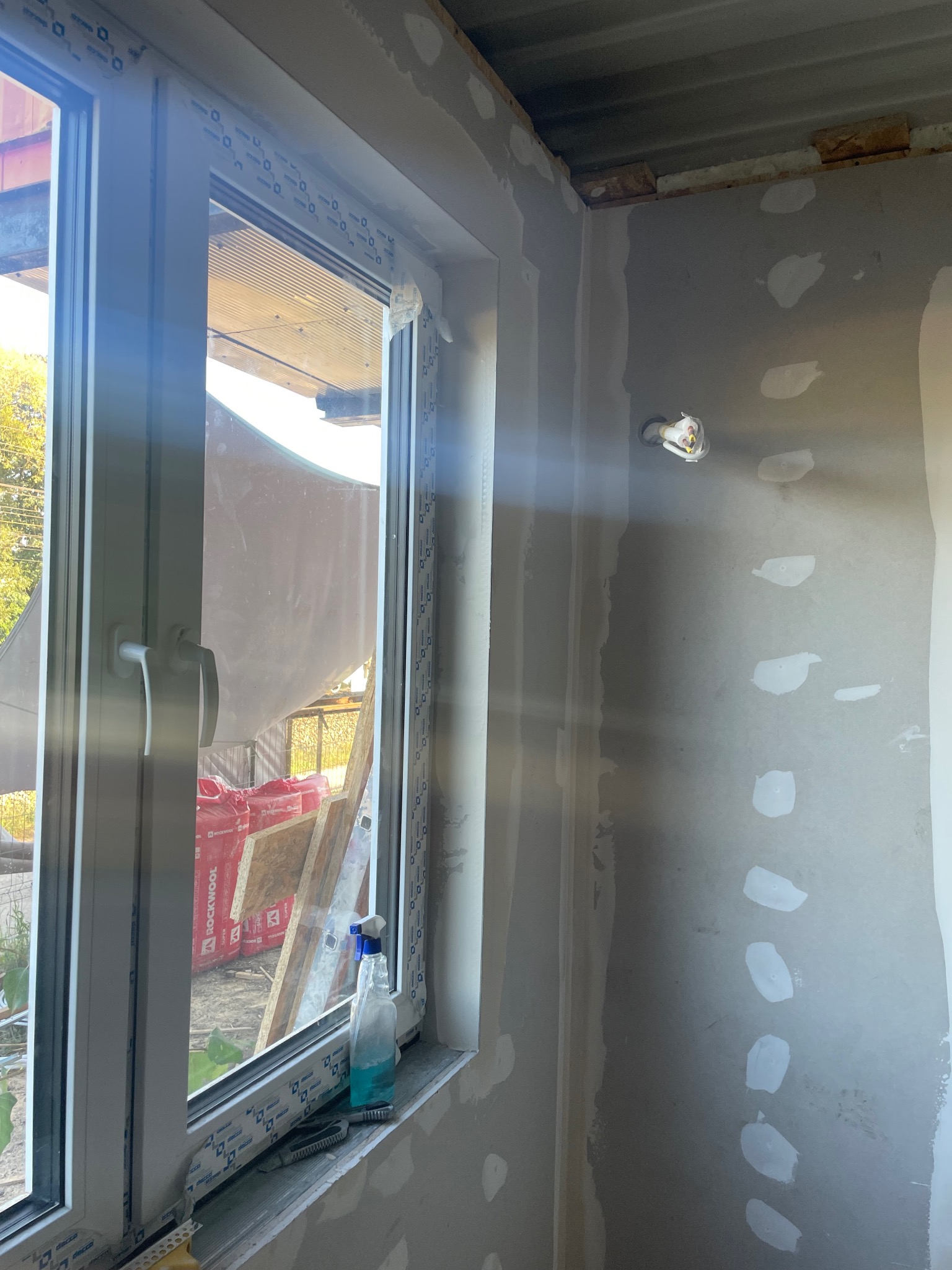 Wnętrze w trakcie szpachlowania ścian, widoczne nowe okno PCV, narzędzia na parapecie i przygotowane ściany do malowania. Etap prac wykończeniowych.