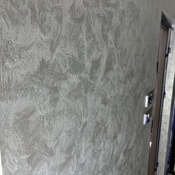 Perfekt Efekt - Dekoracyjna, srebrzysta ściana z efektem szczotkowania, widoczne detale faktury. Fragment futryny drzwiowej z niebieską taśmą malarską w prawym górnym rogu.