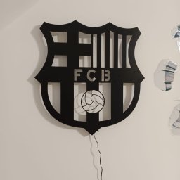 Tomasz Wójcik - Czarny, ażurowy herb FCB z piłką, wykonany z metalu, podświetlony, zawieszony na białej ścianie. Precyzyjne cięcie, nowoczesny design.