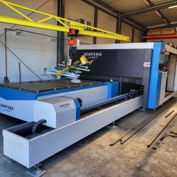 Tomasz Wójcik - Laserowa maszyna CNC Senfeng z żółtym suwnicą i przyssawkami, gotowa do obróbki metalu w hali produkcyjnej. Widoczne profile metalowe na podłodze.