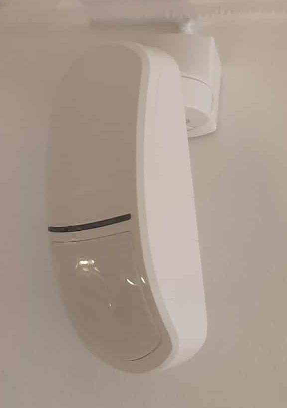 Zamontowany na ścianie czujnik ruchu systemu alarmowego Satel, widoczny z bliska, z delikatnym oświetleniem.