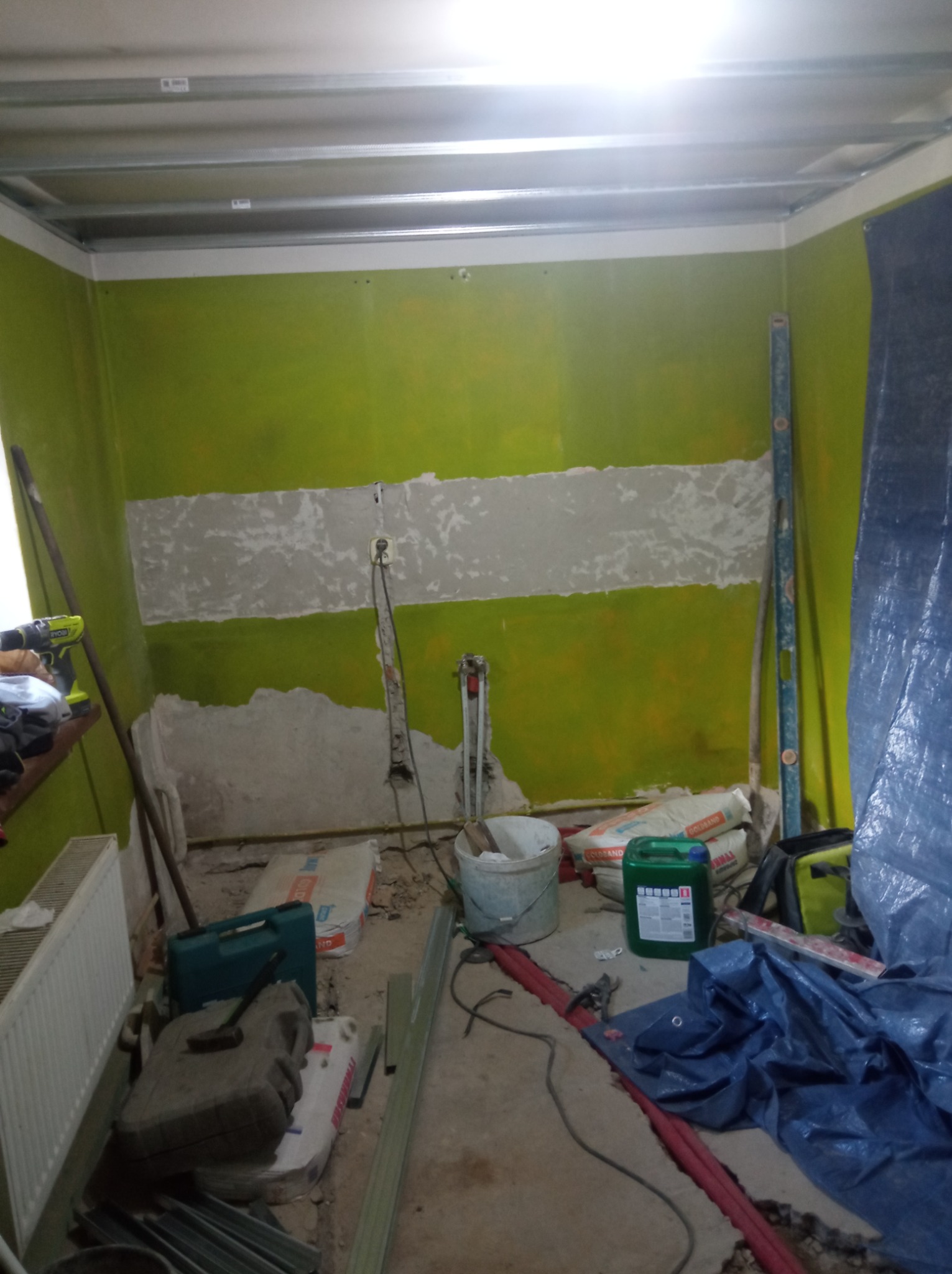 Remont pokoju: zielone ściany z pasem szpachli, profile sufitowe, narzędzia i materiały budowlane na podłodze. Widoczne kable i rury.