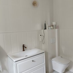 Renova - Jasna łazienka po remoncie: białe płytki, umywalka z szafką, toaleta podwieszana, marmurowe płytki podłogowe i dekoracyjny element na ścianie.