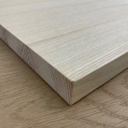 STOLARNIA MODŁA SPÓŁKA Z OGRANICZONĄ ODPOWIEDZIALNOŚCIĄ - Jasny, drewniany blat z widocznym usłojeniem, sfotografowany pod kątem, ukazujący krawędź i fakturę materiału na tle drewnopodobnej powierzchni.