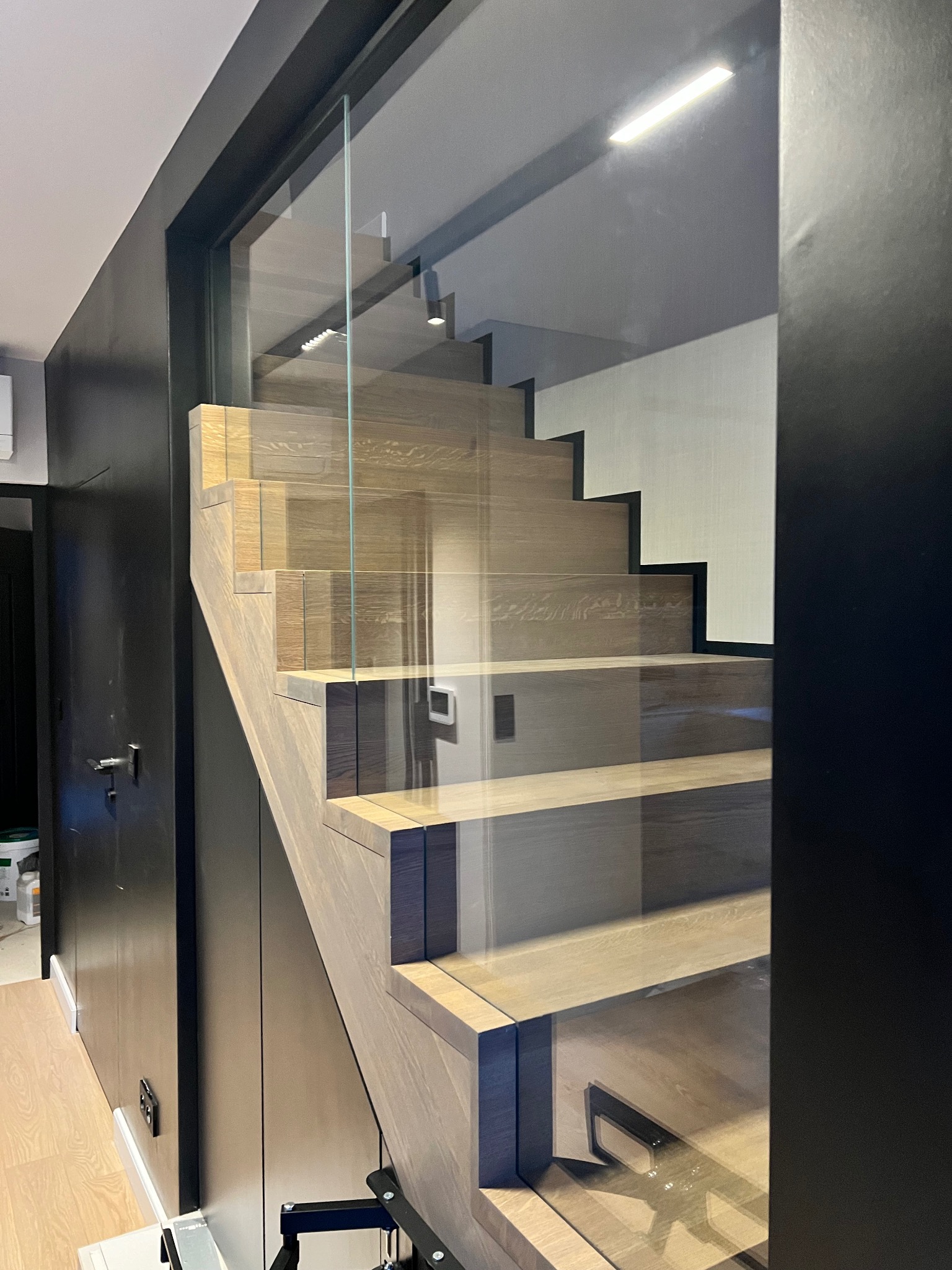 Nowoczesne schody z drewnianymi stopniami i szklaną balustradą, w minimalistycznym wnętrzu w Staniątkach. Widok z dołu, podkreślający detale wykończenia.