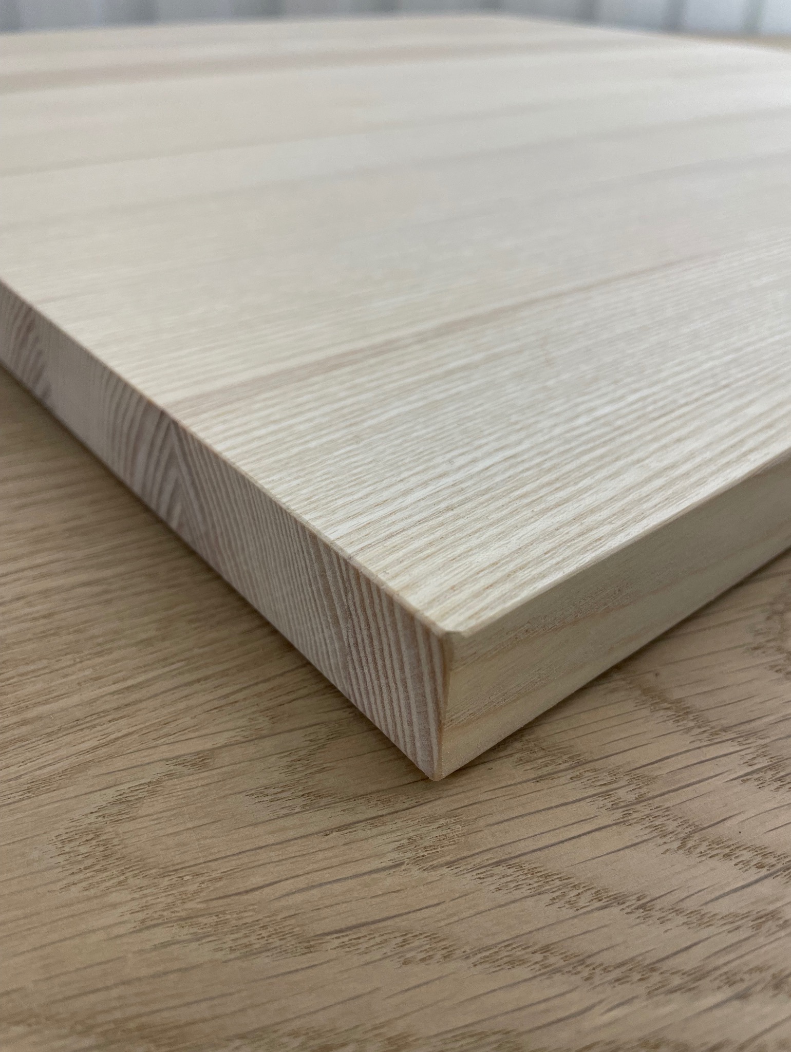 Jasny, drewniany blat z widocznym usłojeniem, sfotografowany pod kątem, ukazujący krawędź i fakturę materiału na tle drewnopodobnej powierzchni.