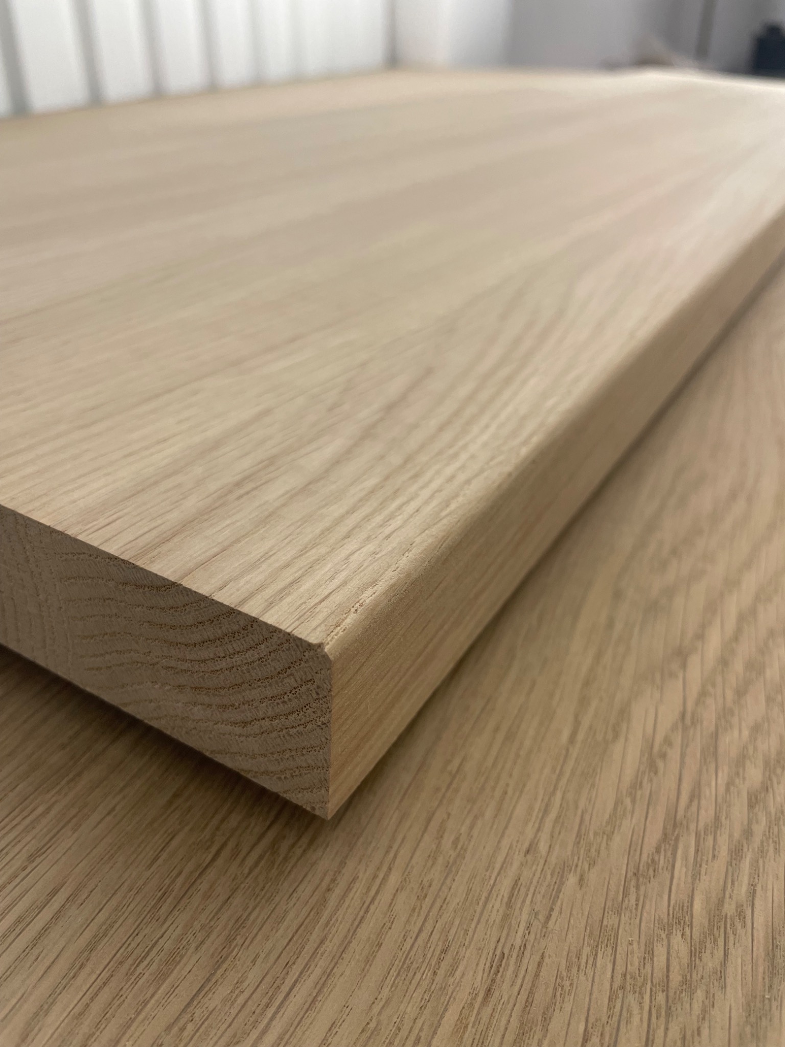 Fragment blatu z jasnego drewna dębowego z zaokrąglonym kantem, ukazujący strukturę słojów. Detal wykończenia meblowego w zbliżeniu.