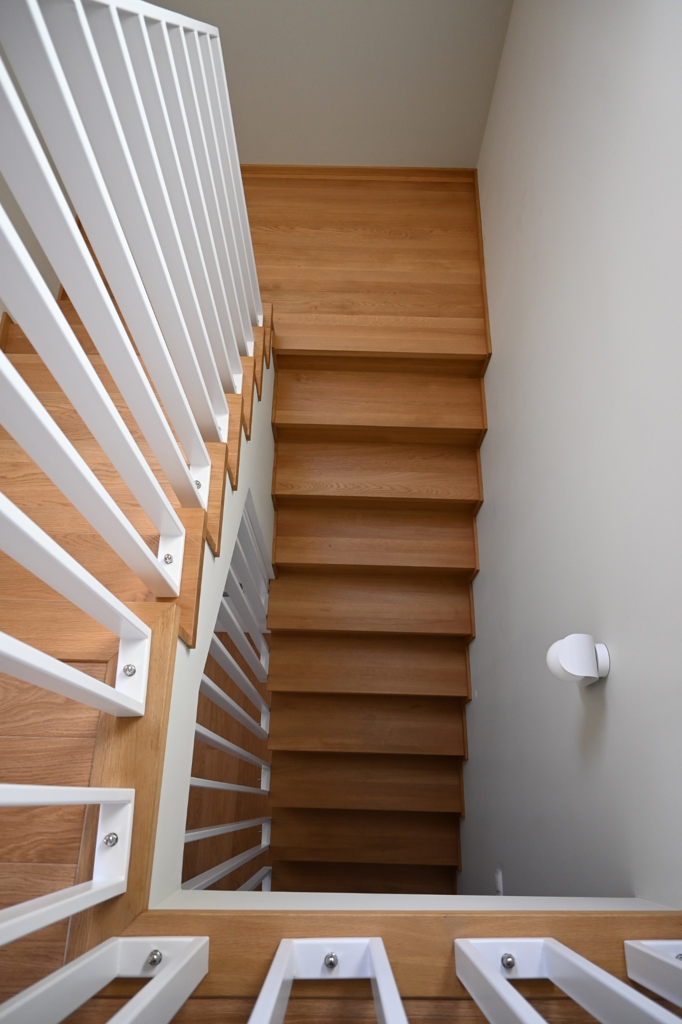 Nowoczesne schody z jasnego drewna z białą, minimalistyczną balustradą, widziane z góry. Naturalne oświetlenie podkreśla strukturę drewna i czystość formy.