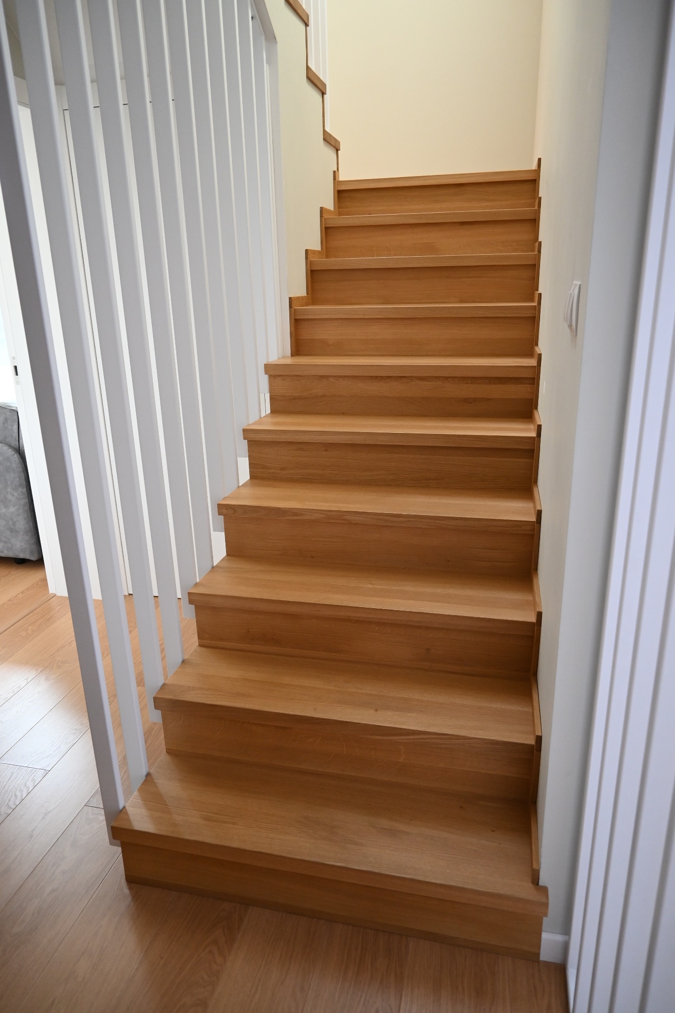 Jasne, drewniane schody z białymi, pionowymi balustradami w nowoczesnym wnętrzu. Widok z dołu, ukazujący detale stopni i minimalistyczny design.