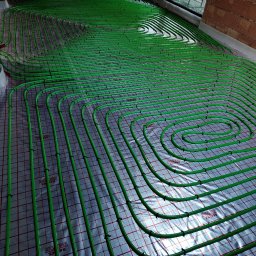 Gaga - Zielone rury ogrzewania podłogowego ułożone spiralnie na folii z siatką, widok z góry, surowy stan przed wylewką. Instalacja w nowym budownictwie.