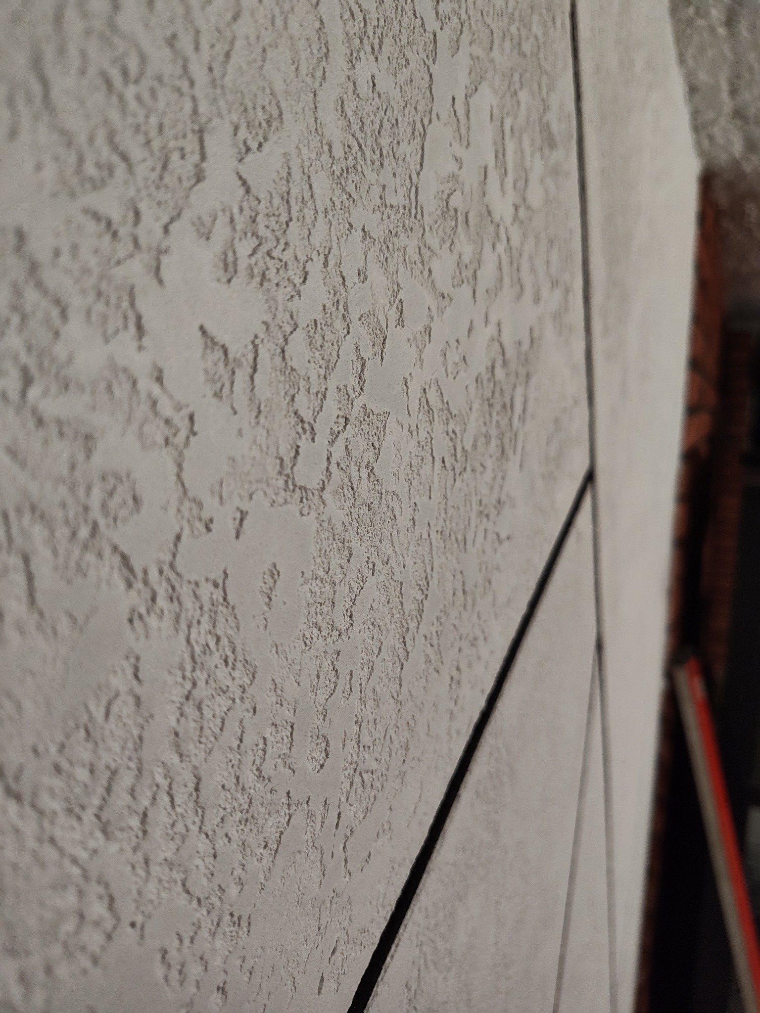 Szara ściana z wyraźną fakturą, imitująca tynk strukturalny, z widocznymi liniami podziału na panele. Ujęcie z boku, podkreślające trójwymiarowość powierzchni.