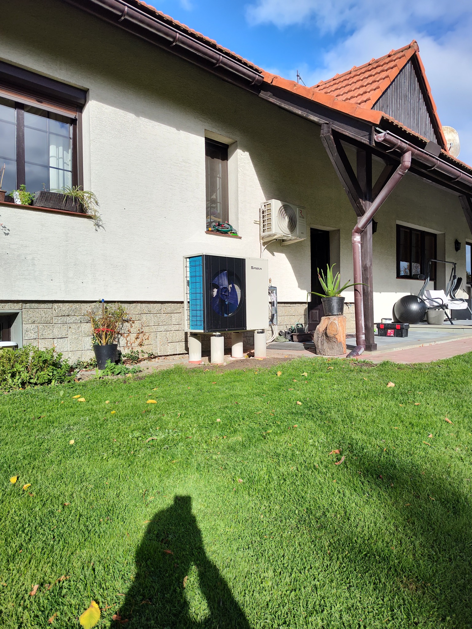 Pompa ciepła zamontowana przy domu jednorodzinnym w Ślemieniu. Widoczny trawnik, elewacja budynku i okna. Instalacja wykonana na zewnątrz budynku.