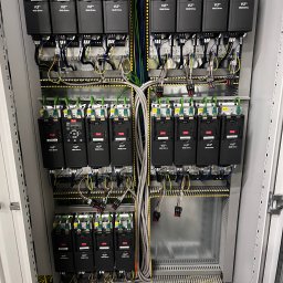 Karol Brożek - Rozdzielnica elektryczna z zamontowanymi falownikami Danfoss VLT Midi Drive, widoczne liczne przewody i złącza. Układ symetryczny, uporządkowany w szafie sterowniczej.