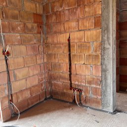 Karol Brożek - Wewnętrzne ściany z cegły z widocznymi, częściowo zamontowanymi przewodami elektrycznymi w peszlach i puszkach instalacyjnych. Surowy stan wykończenia.