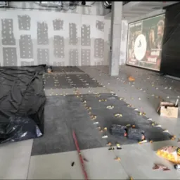 Układanie ciemnych płytek podłogowych w dużym pomieszczeniu z użyciem poziomicy i krzyżyków dystansowych. Ściany przygotowane do gładzi.