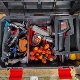 TBR RYSZARD ZWIERZYCKI - Otwarta czarna skrzynka narzędziowa z precyzyjnie ułożonymi narzędziami elektrycznymi: czerwono-żółte wkrętaki izolowane, miernik termowizyjny Sonel KT-256-PRO i kable, widoczna z góry.