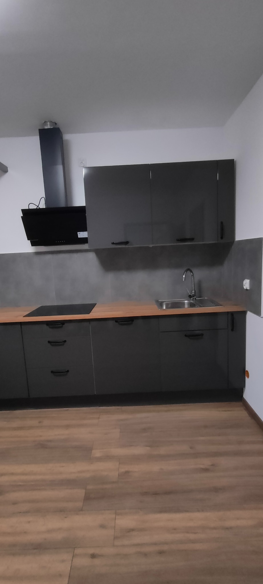 Nowoczesna, szara kuchnia z drewnianym blatem i czarnym okapem. Minimalistyczny design, widok na podłogę z paneli. Ujęcie z niskiego kąta.