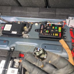 Czyścioch z dojazdem Mobilne sprzatanie - Diagnostyka elektryczna auta: ręka w rękawicy trzyma uszkodzony bezpiecznik na tle skrzynki bezpieczników i akumulatora w bagażniku BMW.