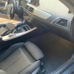 Wnętrze samochodu BMW po czyszczeniu: czarne fotele, deska rozdzielcza z srebrnymi akcentami, czysta podłoga. Widok z otwartymi drzwiami.