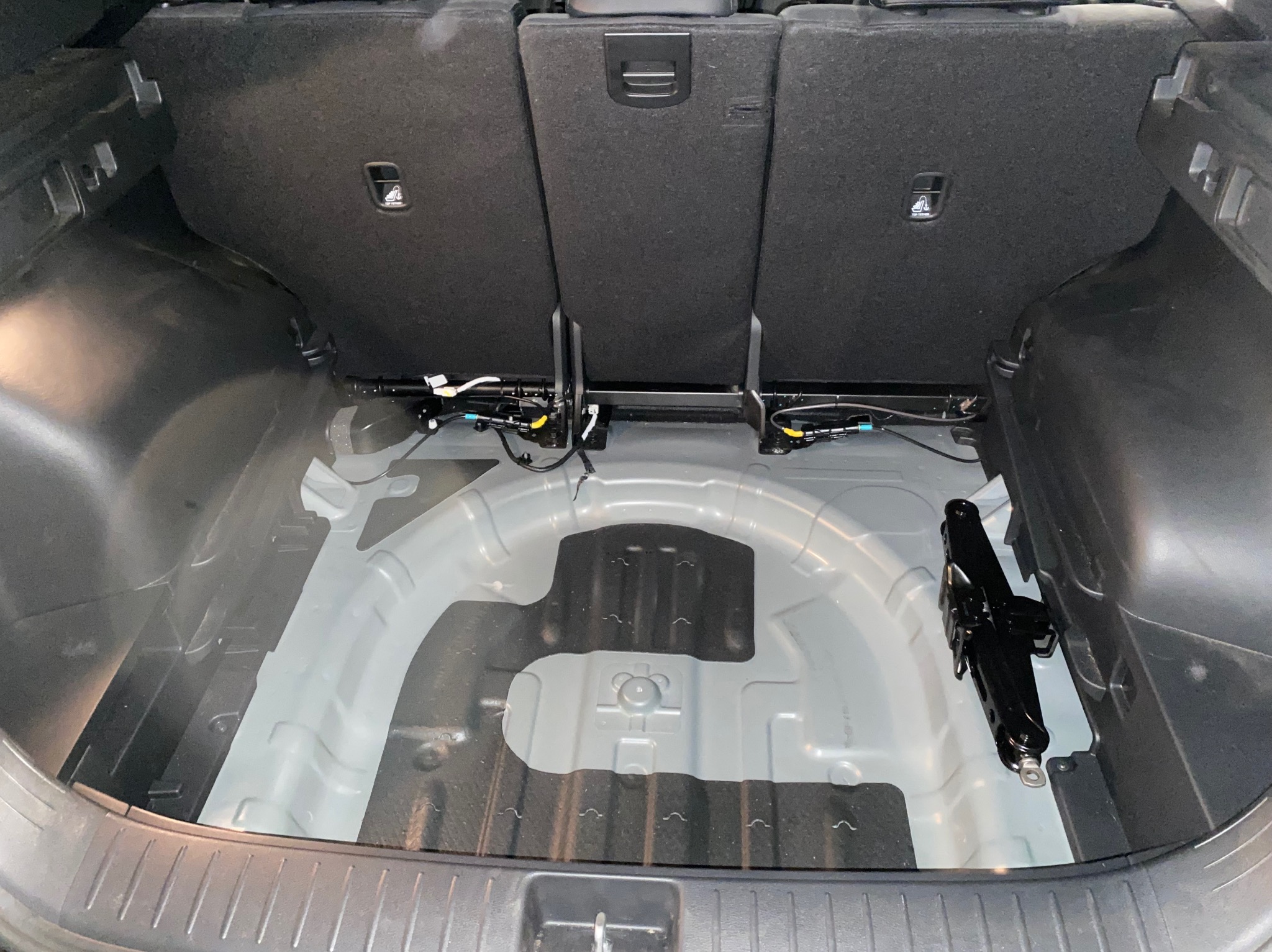 Pusty bagażnik samochodu z podniesionymi siedzeniami, widoczny podnośnik i elementy instalacji elektrycznej. Czyste wnętrze, gotowe do załadunku.