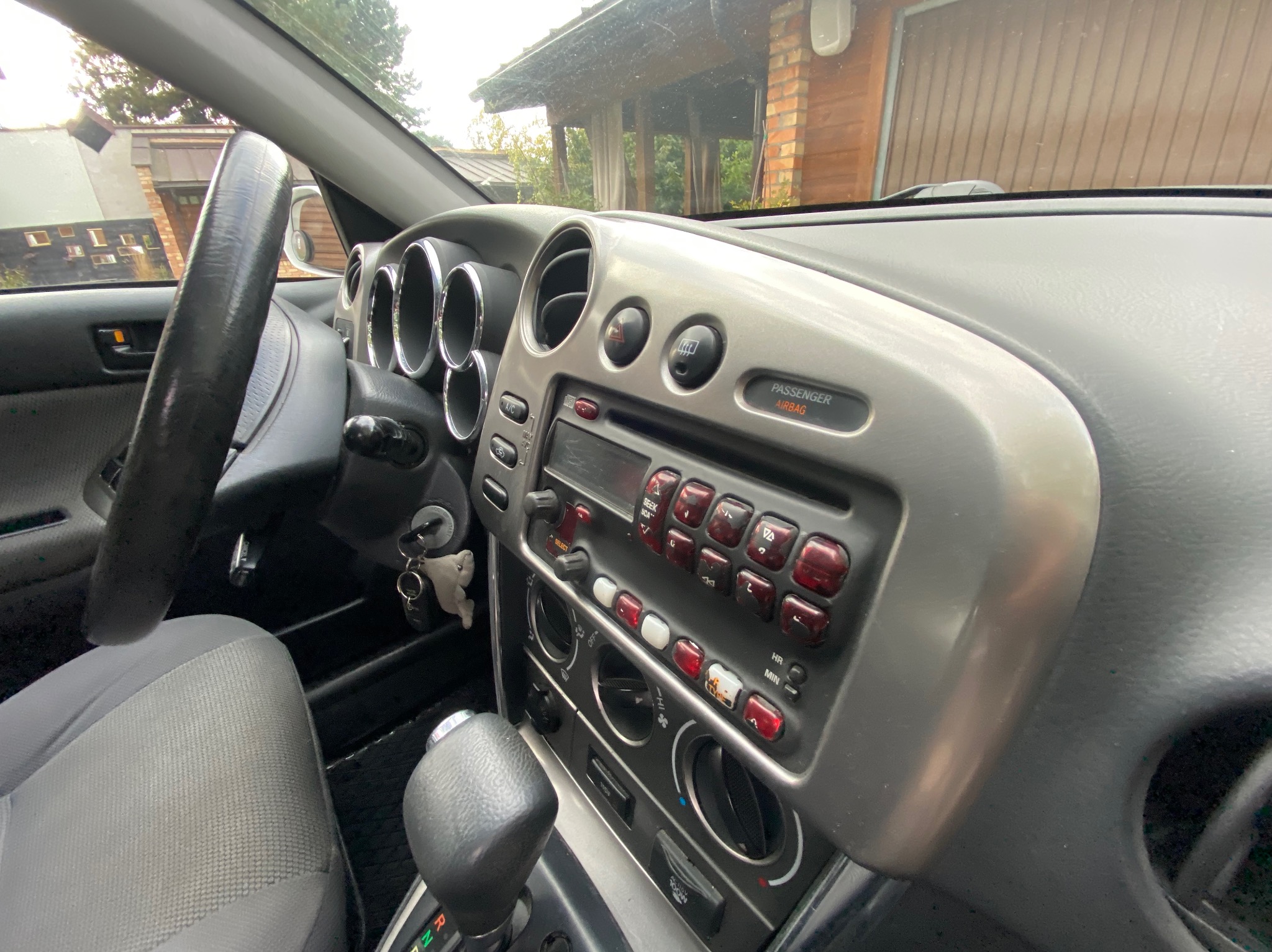 Wnętrze samochodu z widoczną deską rozdzielczą, kierownicą i siedzeniem kierowcy. Widoczne elementy sterowania i przyciski. Ujęcie z perspektywy kierowcy.