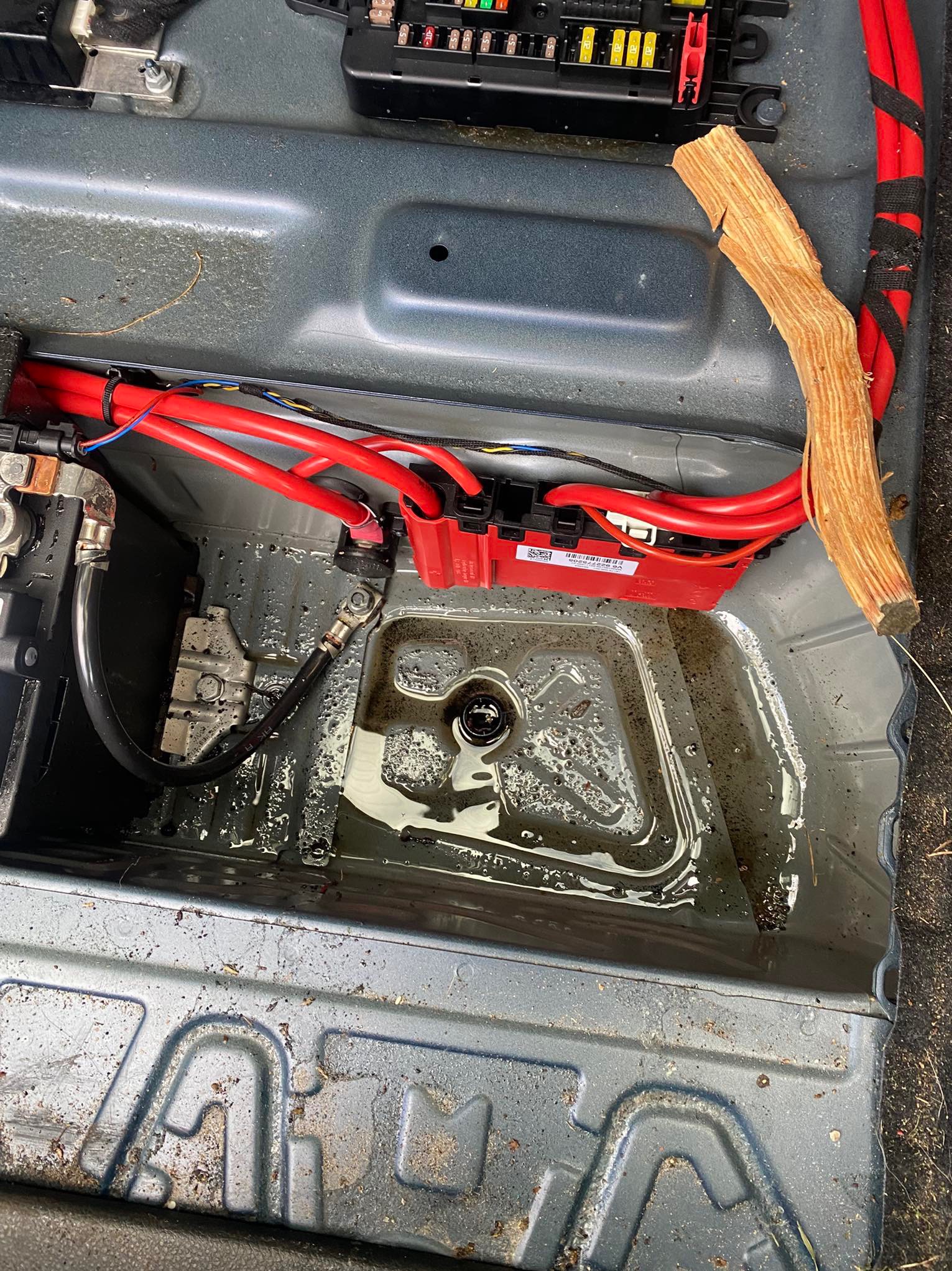 Zalana woda w bagażniku samochodu z widocznymi przewodami elektrycznymi i elementami instalacji. Widoczne zabrudzenia i pozostałości po zalaniu.