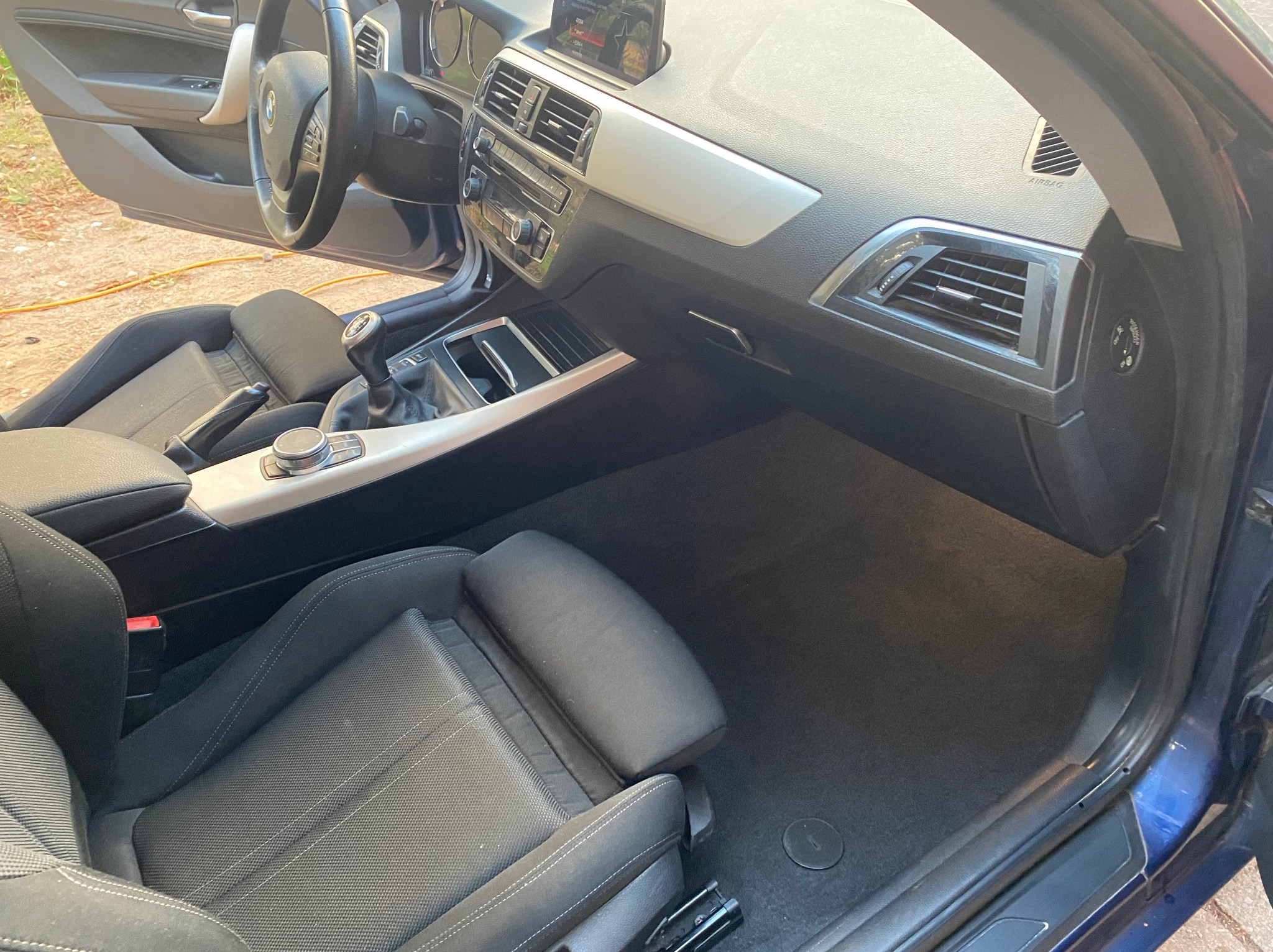 Wnętrze samochodu BMW po czyszczeniu: czarne fotele, deska rozdzielcza z srebrnymi akcentami, czysta podłoga. Widok z otwartymi drzwiami.