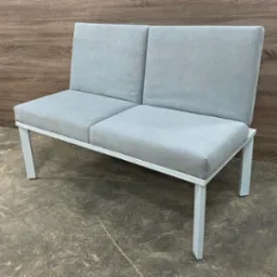 Nowoczesna, dwuosobowa sofa z szarą tapicerką i białą, metalową ramą na tle drewnianej ściany i betonowej podłogi. Minimalistyczny design, proste linie.