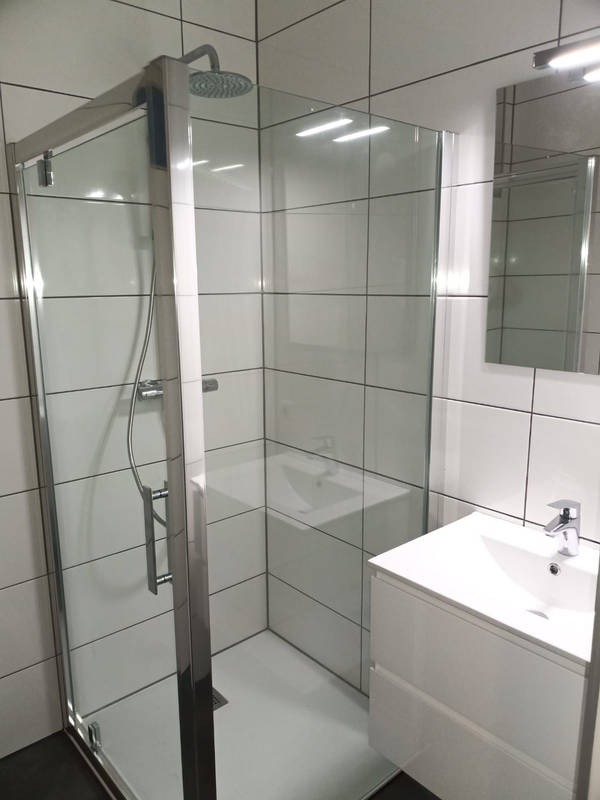 Nowoczesna kabina prysznicowa ze szklanymi drzwiami i białą armaturą w łazience wyłożonej białymi płytkami. Minimalistyczny design, chromowane wykończenia.