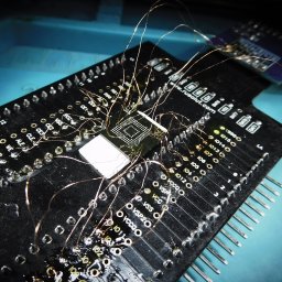 SGdata Krzysztof Dołhan - Mikroskopijne połączenia na czarnej płytce drukowanej z układem scalonym, prawdopodobnie w trakcie zaawansowanego procesu inżynieryjnego lub diagnostycznego.