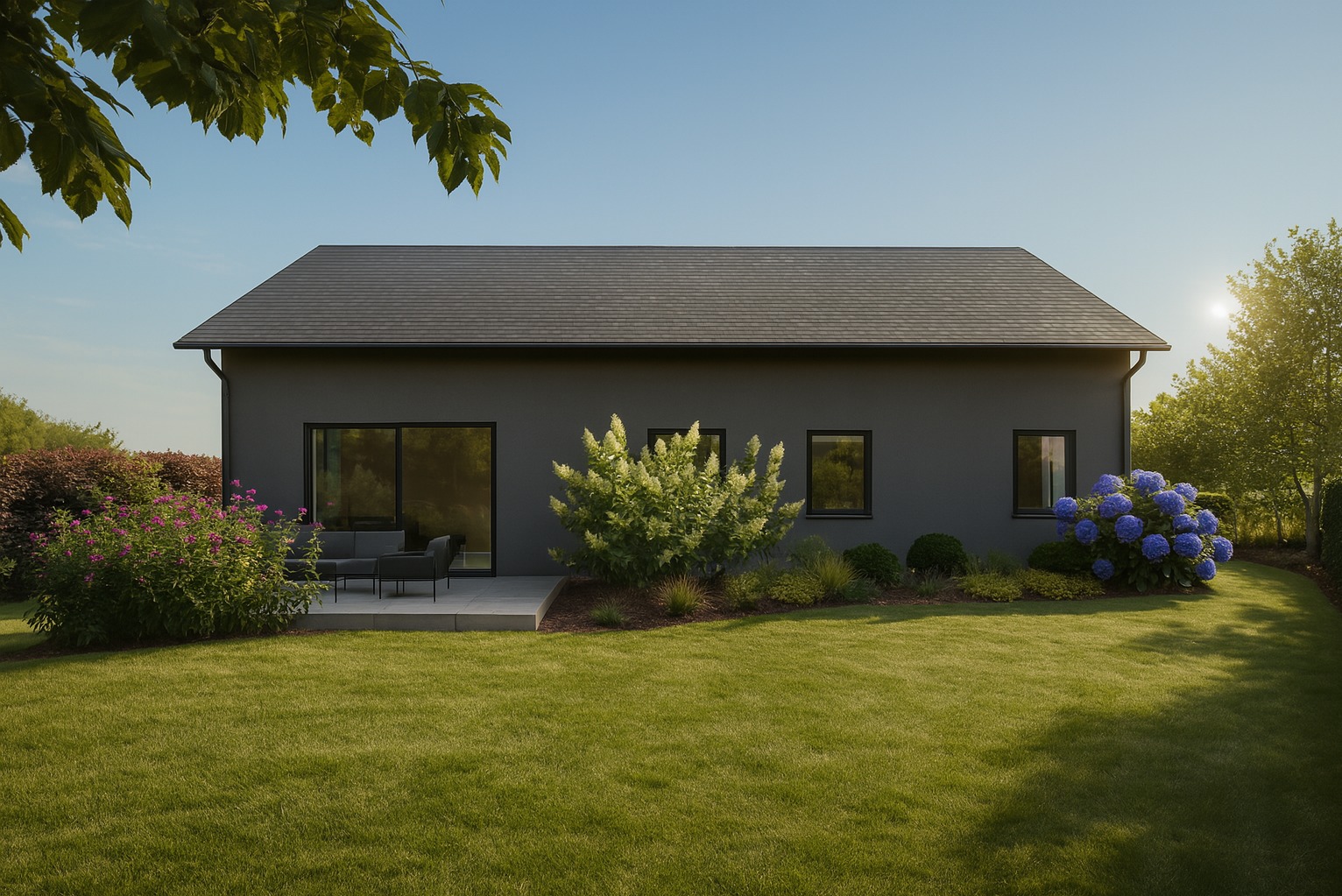 Nowoczesny dom z szarą elewacją i zadbanym trawnikiem. Hortensje, krzewy i drzewa tworzą harmonijną kompozycję ogrodu. Minimalistyczny taras z meblami.