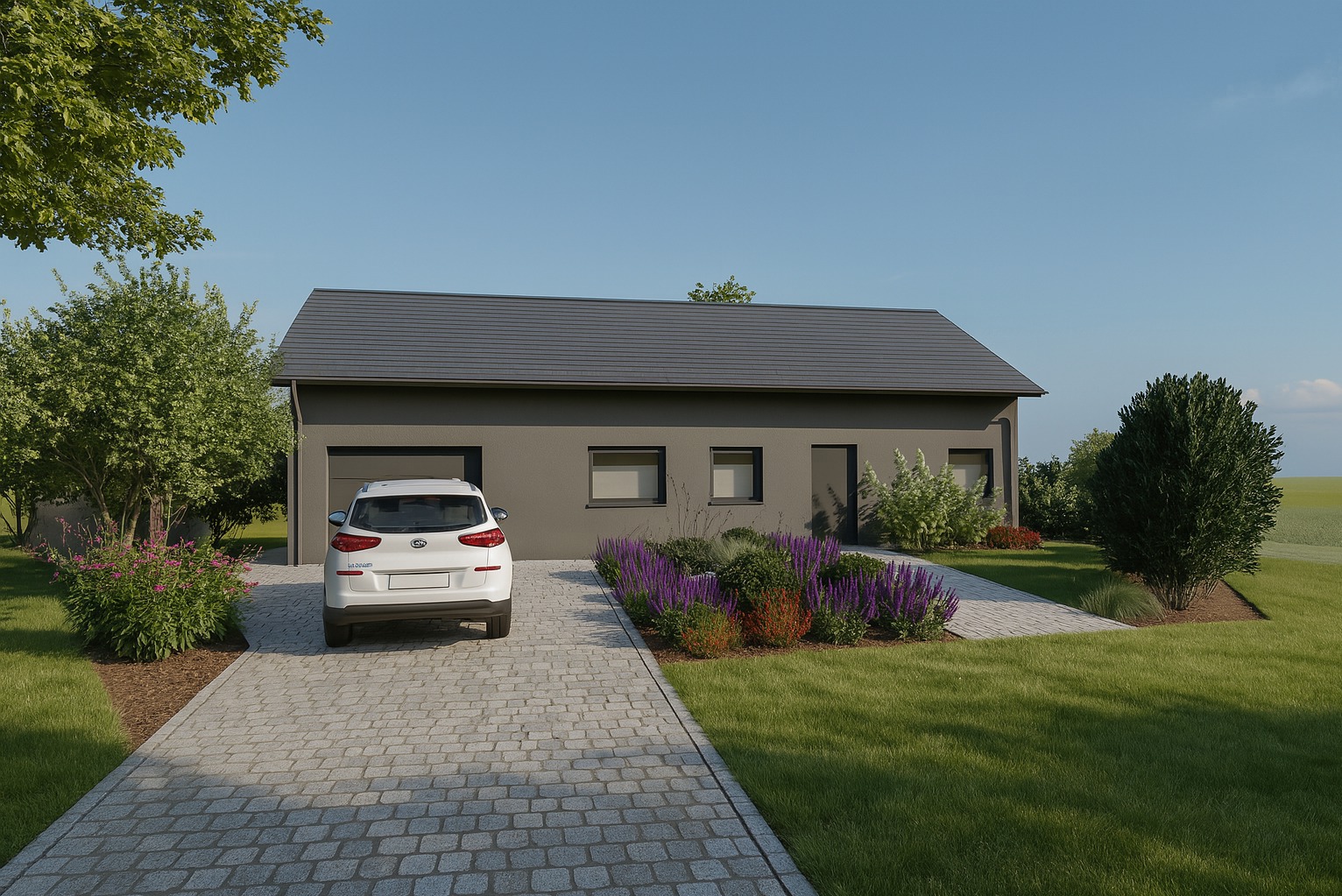 Nowoczesny dom z szarą elewacją, podjazdem z kostki i rabatami z kwitnącymi, fioletowymi kwiatami. Biały samochód zaparkowany przed garażem.