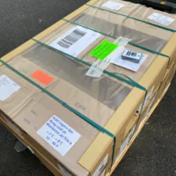 Paleta z kartonami WK3, zabezpieczona folią i taśmami, z etykietami informacyjnymi i urządzeniem do pomiaru temperatury, gotowa do transportu.